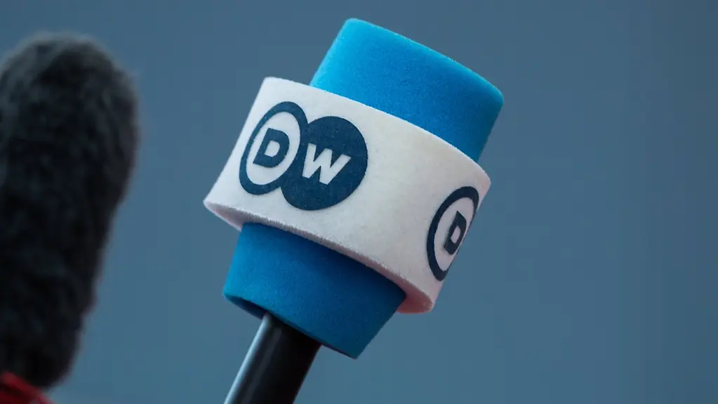 Ein blaues Mikrophon mit einer weißen Binde, auf der der Schriftzug "DW" zu sehen ist.