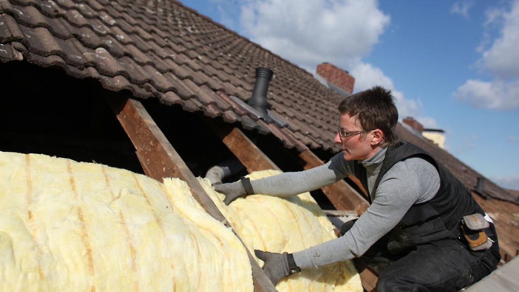 Ein Bauingeneurin und Dachdeckerin verlegt in Köln Mineralwolle zur Wärmedämmung auf einem Dach eines Hauses.