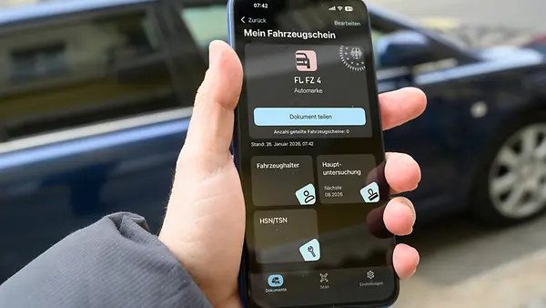 Ein Mann hält ein Smartphone in der Hand auf dem der digitale Fahrzeugschein angezeigt wird