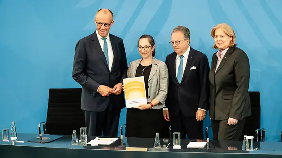Bundeskanzler Merz und Ministerin Bas stehen mit Frank-Jürgen Weise und Constanze Janda in der Regierungspressekonferenz und halten den Bericht der Alterssicherungskommission in den Händen.