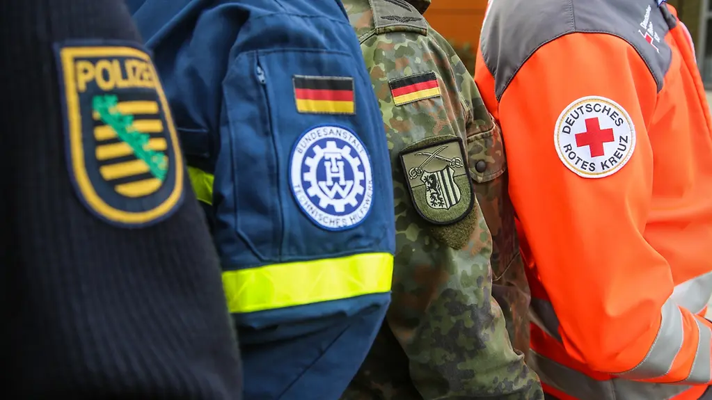 Nahaufnahme der Abzeichen an den Uniformen der teilnehmenden Organisationen bei einer zivil-militärischen Zusammenarbeit der Bundeswehr mit verschiedenen Organisationen.