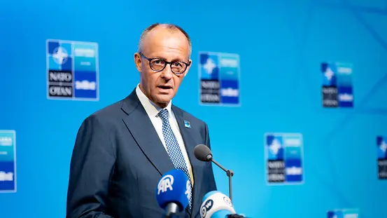 Bundeskanzler Merz vor blauer Wad mit NATO-Kogos.