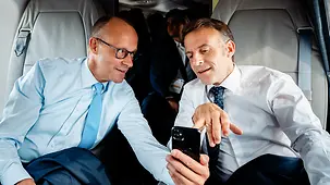 Merz and Macron in the helicopter, both looking at the Chancellor’s smartphone
