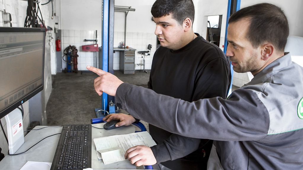 Can Bilgic, Auszubildender zum KfZ-Mechatroniker (links) und Murat Aslan, Inhaber des Autodienstes Löwe in Berlin in der Werkstatt vor einem Computer am Bildschirm.