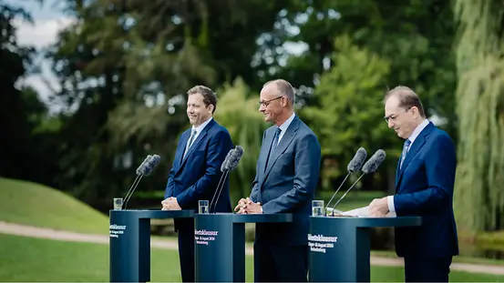 Bundeskanzler Merz steht gemeinsam mit Vizekanzler Klingbeil und Bundesinnenminister Dobrindt hinter drei Pulten bei der Abschlusspressekonferenz der Kabinettsklausur im Garten des Schlosses Neuhardenberg.