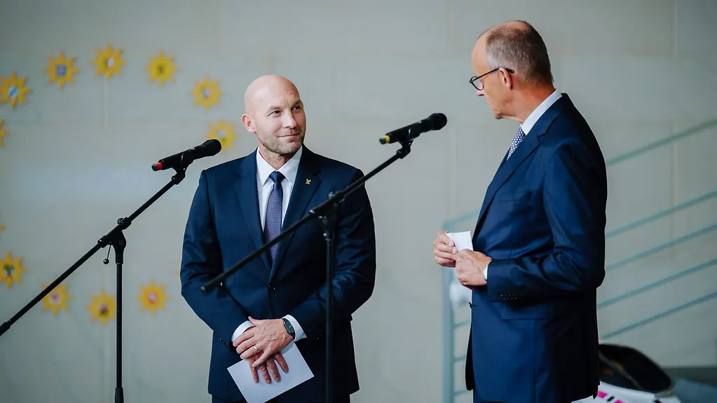 Bundeskanzler Friedrich Merz steht neben Ronald Rauhe.