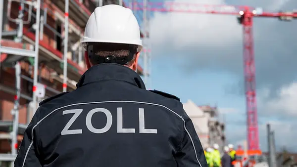 Eine Einsatzkraft des Zolls steht vor einer Baustelle.