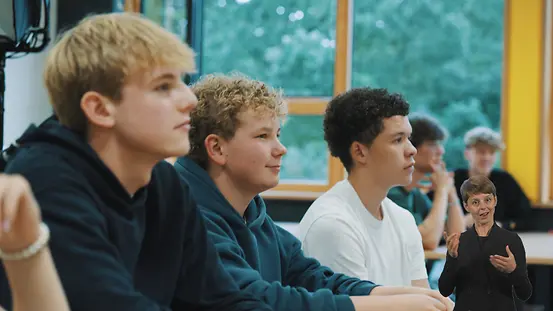 Schülerinnen sitzen in einem Klassenraum und schauen nach vorne in Richtung des Lehrpersonals