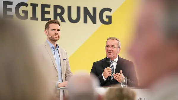 Bundesverteidigungsminister Boris Pistorius und Moderator am Rednerpult im Dialogforum der Bundesregierung