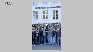 Bundeskanzler Merz mitten in einer Gruppe von Schülerinnen und Schülern vor dem Friedrich-Spee-Gymnasium.