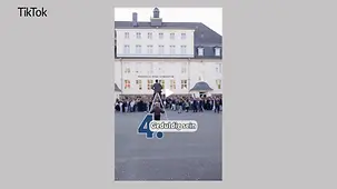 Ein Fotograf auf einer Klappleiter vor der Gruppe aus Schülerinnen und Schülern und dem Kanzler vor dem Gymnasium. Eine Frau sichert die Leiter.