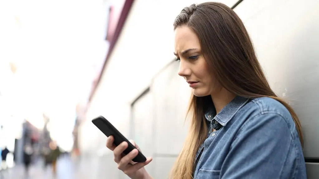 Profil einer traurigen Frau, die auf der Straße Online-Inhalte von Smartphones überprüft.