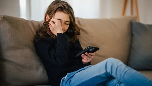 Ein junges Mädchen liest eine beleidigende SMS – sie ist Opfer von Cybermobbing. 