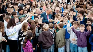 Bundeskanzler Friedrich Merz umringt von Schülerinnen und Schülern.