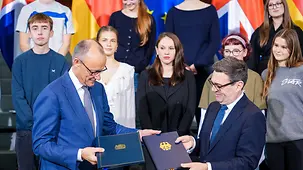 Bundeskanzler Friedrich Merz und der britische Premierminister tauschen Dokumentenmappen aus.