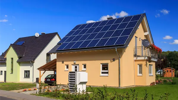 Niedrigenergie-Einfamilienhaus mit Solaranlage auf dem Dach und Luftwärmepumpe im Vorgarten.