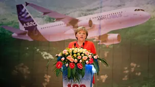 Angela Merkel speaks; behind her the photo of an Airbus.