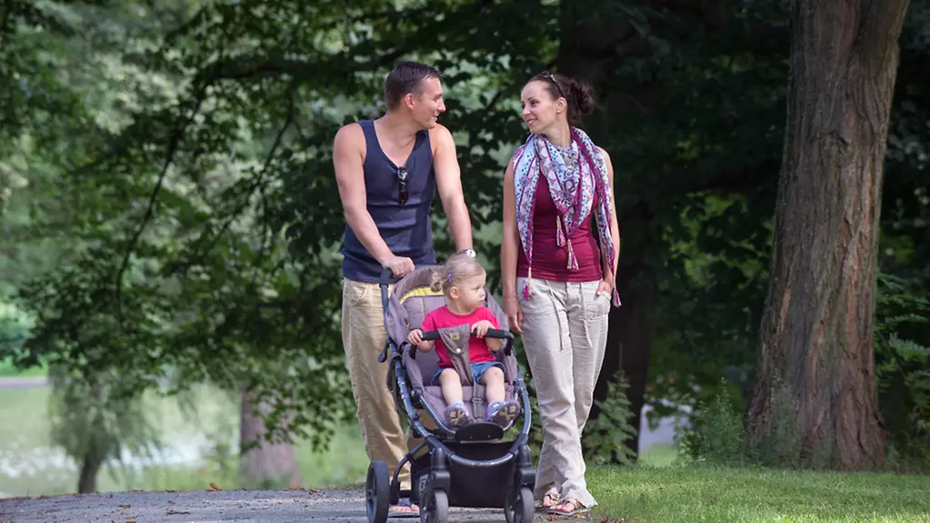 Eine junges Elternpaar wandert mit seiner kleinen Tochter im Kinderwagen durch einen Park am Orankesee in Berlin.