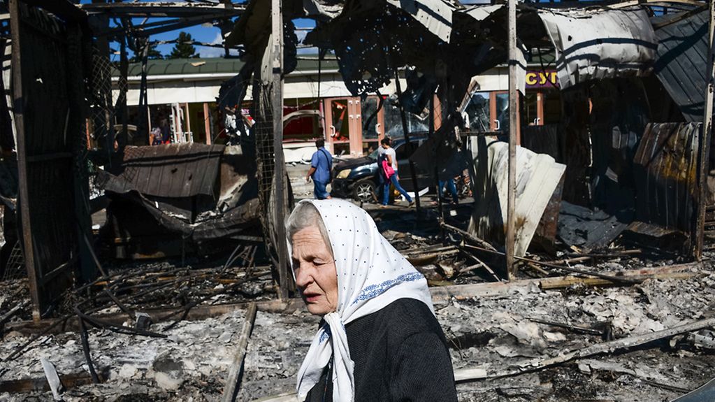 An elderly woman passes ruined buildings in the Ukrainian town of Donetsk