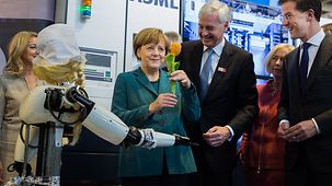 Chancellor Angela Merkel next to a robot in traditional Dutch dress at the Holland High Tech stand
