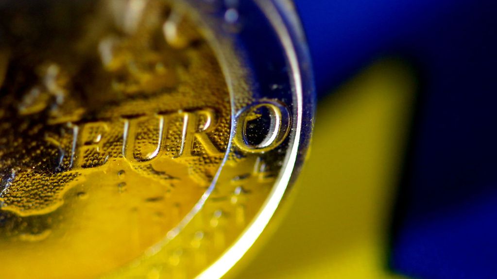 Eine Euro-Münze steht auf einer EU-Fahne.