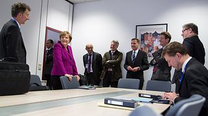 Dans un bureau, la chancelière fédérale Angela Merkel en compagnie de ses conseillers et d’autres membres de sa délégation