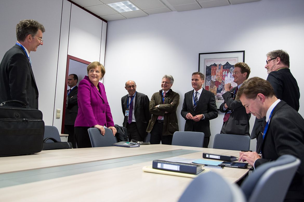 Dans un bureau, la chancelière fédérale Angela Merkel en compagnie de ses conseillers et d’autres membres de sa délégation
