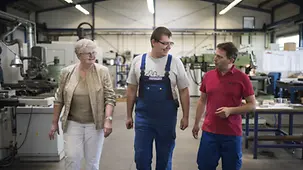 Hannelore Keunecke, Ausbilder Lars Uhlmann und Marcel Graupner laufen durch die Werkhalle.