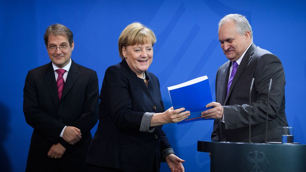 Bundeskanzlerin Angela Merkel bekommt den Jahresbericht zur Begutachtung der gesamtwirtschaftlichen Entwicklung aus der Hand von Christoph M. Schmidt.