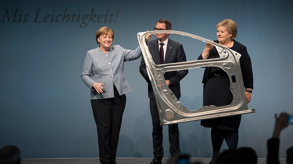 Bundeskanzlerin Angela Merkel und Norwegens Ministerpräsidentin Erna Solberg halten eine Autotür im Rahmen eines Rundgangs durch die neue Produktionsanlage der Firma Hydro Aluminium Deutschland GmbH.