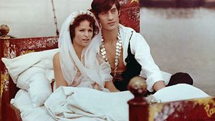 Hauptdarsteller Angelika Domröse und Winfried Glatzeder sitzend in einem Bett, dass sich scheinbar auf einem Schiff befindet, Domröse mit einem Schleier in den Haaren