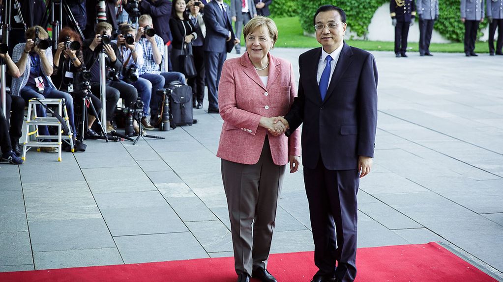 Chancellor Angela Merkel and China's Prime Minister Li Keqiang shake hands - behind them a bank of photographers with cameras.