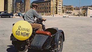 Horst Buchholz mit einem Motorrad, am Beiwagen steht: Russki go home