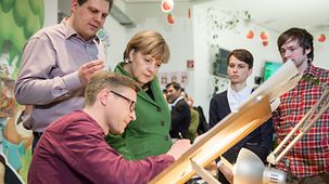 Beeindruckt verfolgt Bundeskanzlerin Angela Merkel, wie ein Illustrator am Zeichentisch arbeitet.