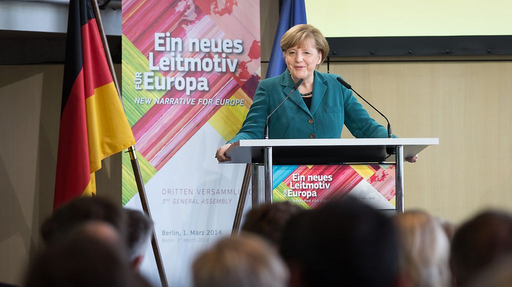 Merkel hält eine Rede, hinter ihr das Logo der Veranstaltung