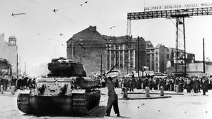 Ein Mann schlägt mit einer Stange auf einen sowjetischen Panzer ein.
