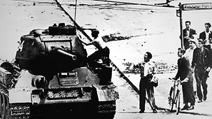 Demonstranten beobachten einen Mann, der auf einen Panzer klettert.