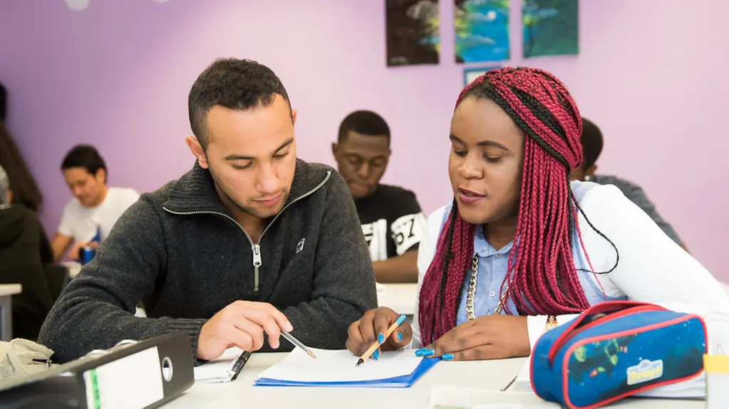 Die Schüler Omid Rezai (links) und Susan Namutebi (rechts) sitzen an einem Tisch in ihrem Klassenraum.