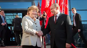 Merkel begrüßt Putin vor Messefahnen.
