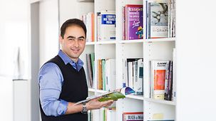 Soroosh Eghbali, Mitarbeiter bei der ModuleWorks GmbH in Aachen steht vor einem Bücherregal in der Unternehmensbibliothek.