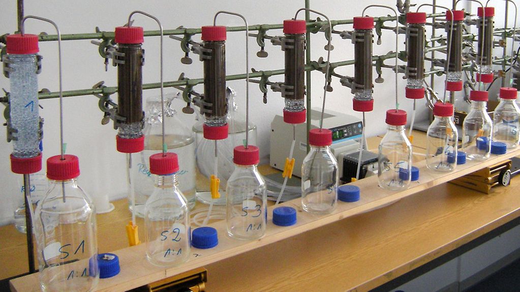 (Säulenversuch): Laborversuch mit Nanopartikeln in Bodenproben. Die Glasröhren werden mit künstlichem Regenwasser durchströmt. Der Ablauf wird in Glasgefäßen für die anschließende chemische Analytik gesammelt.