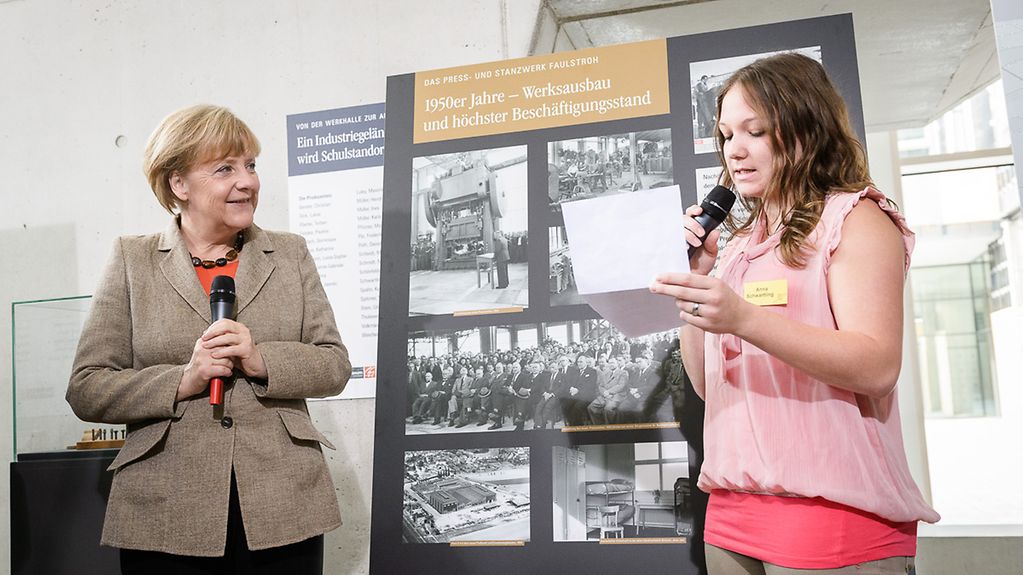 Bundeskanzlerin Angela Merkel hört sich den Vortrag einer Schülerin über ein Geschichtsprojekt an.