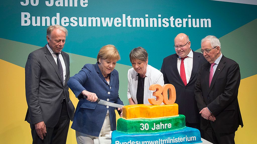 Bundeskanzlerin Angela Merkel, die aktuelle Bundesumweltministerin sowie einige ehemalige Minister schneiden eine Geburtstagstorte an.