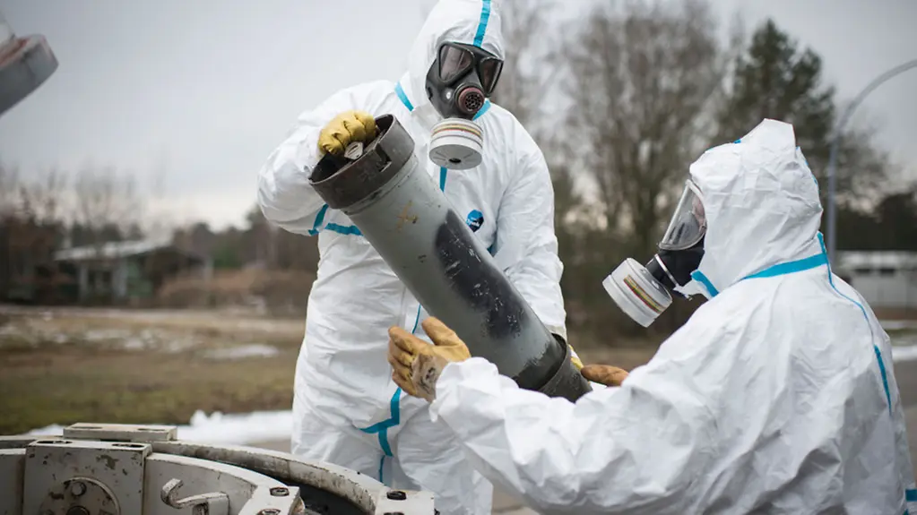 Mitarbeiter der GEKA (Gesellschaft zur Entsorgung von chemischen Kampfstoffen und Rüstungsaltlasten) in Schutzanzügen demonstrieren wie ein Dummy-Gefäß mit angedachten chemischen Kampfstoffen aus einem Transportbehälter entnommen wird.