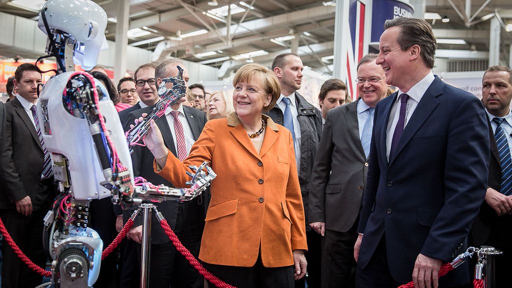 Bundeskanzlerin Angela Merkel und Großbritanniens Premierminister David Cameron beim Rundgang auf der Cebit an einem Stand mit Roboter.