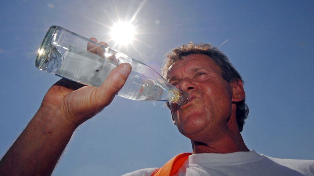 Ein Straßenbauarbeiter trinkt in der Hitze aus einer Wasserflasche.