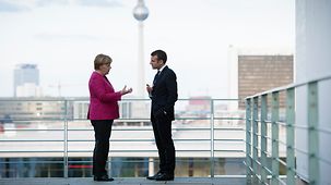 Bundeskanzlerin Angela Merkel unterhält sich mit Frankreichs Präsident Emmanuel Macron auf der Terrasse.