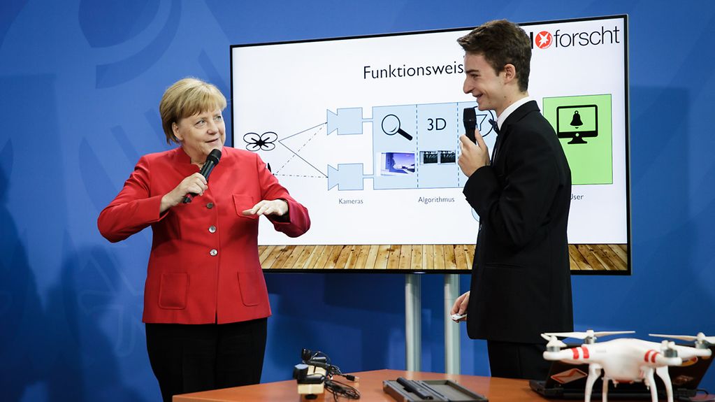 Jugend-forscht-Gewinner Tassilo Schwarz erklärt Bundeskanzlerin Angela Merkel seine von ihm entwickelte Drohnenabwehrtechnik.