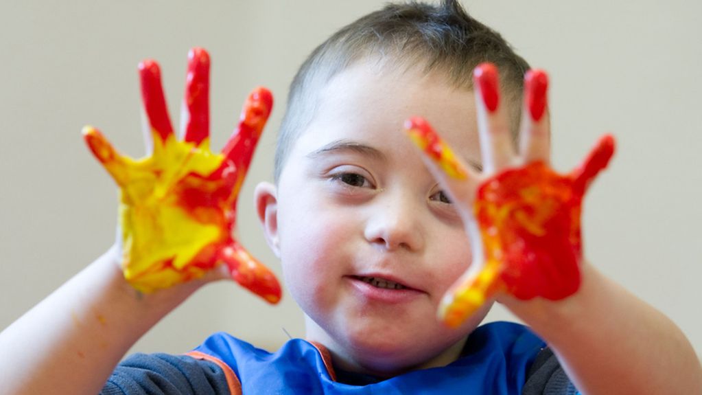 Kleiner Junge mit Down-Syndrom malt mit Fingerfarben.
