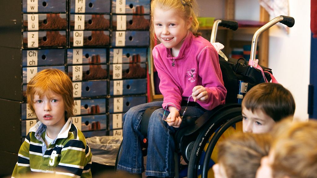 Ein Mädchen im Rollstuhl zwischen ihren nichtbehinderten Mitschülern.